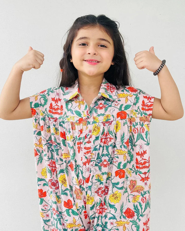 Young girl wearing a colorful floral shirt with her arms raised against a white background