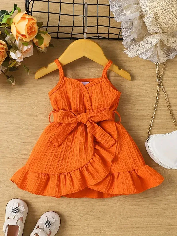 Orange dress with a bow on a wooden surface with flowers and shoes in the background