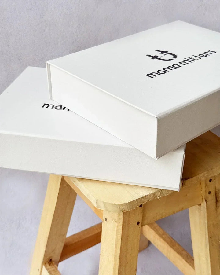 Two white boxes with 'mamamitens' branding on a wooden stool against a gray background