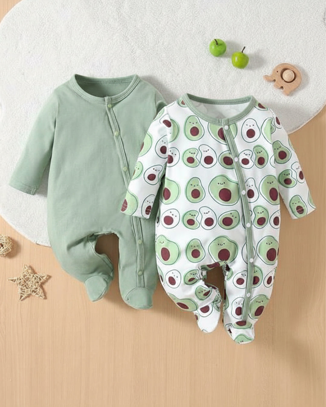 Two baby rompers, one green and one with avocado pattern, on a wooden surface.