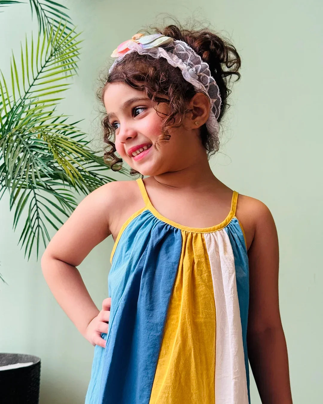 Young girl wearing a colorful dress with a plant in the background