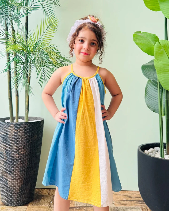 Young girl wearing a colorful dress standing in front of potted plants.