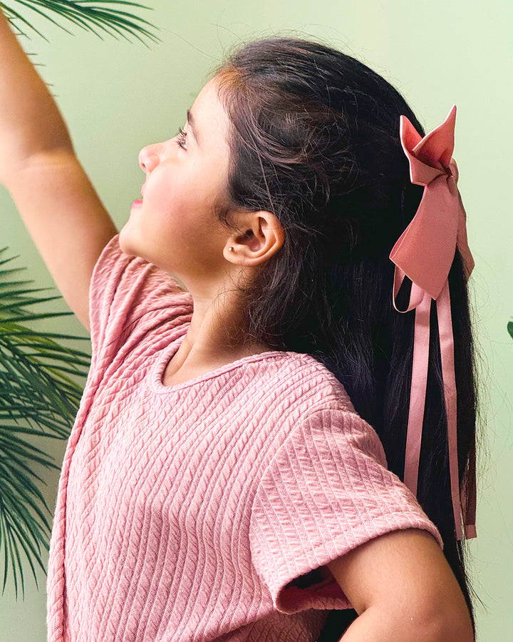 Woman with pink bow in hair wearing a pink textured top against a light green background