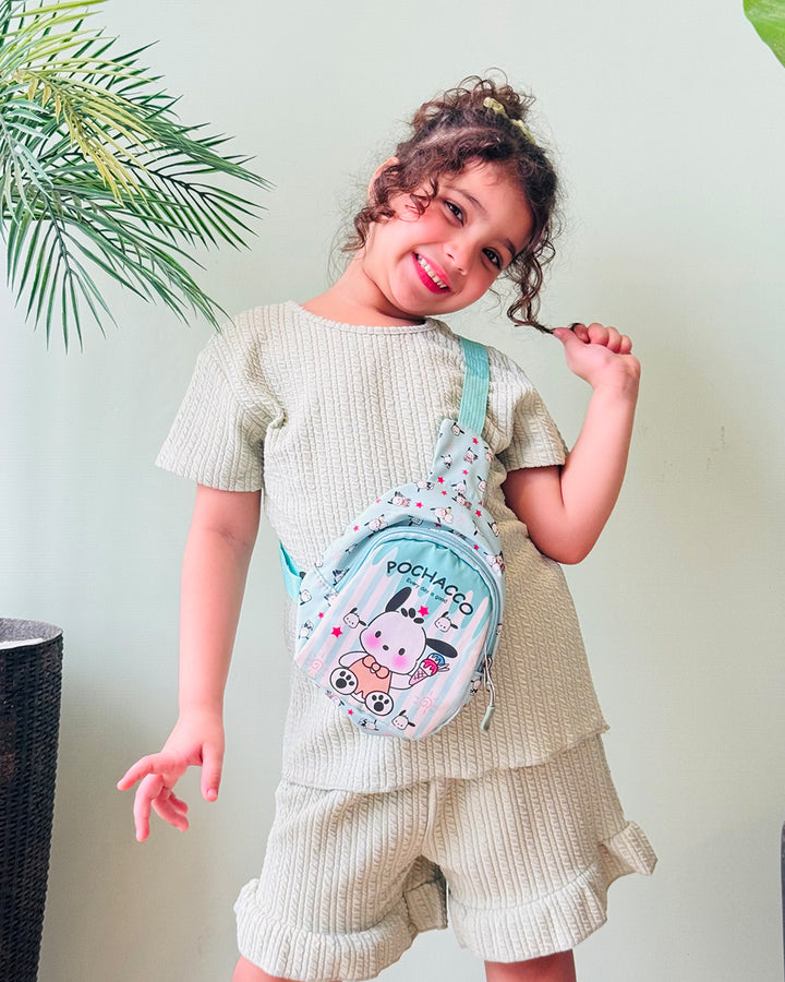 Child wearing a light green top and beige shorts with a small bag, standing against a light background.