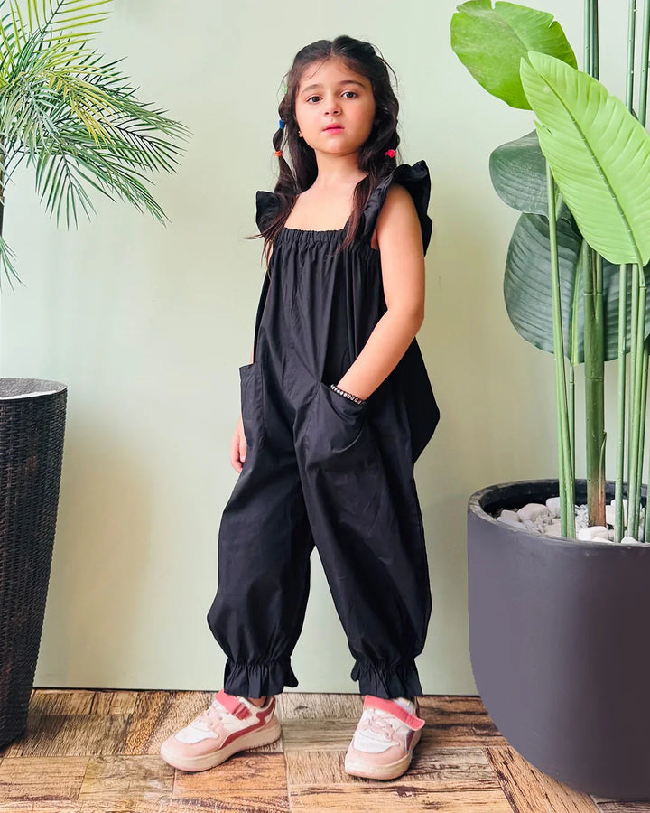 Young girl wearing a black outfit standing between two potted plants.