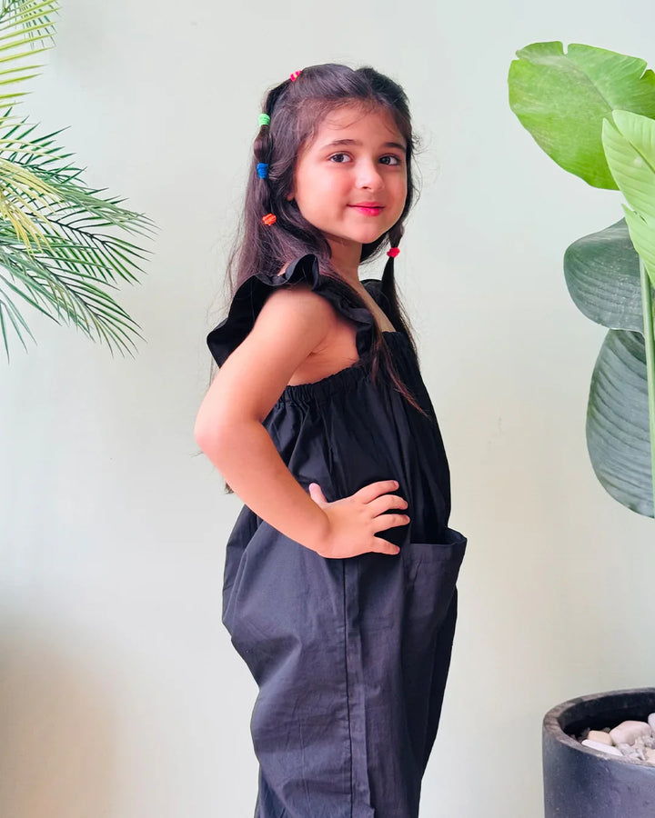 Young girl in a black dress standing in front of green plants
